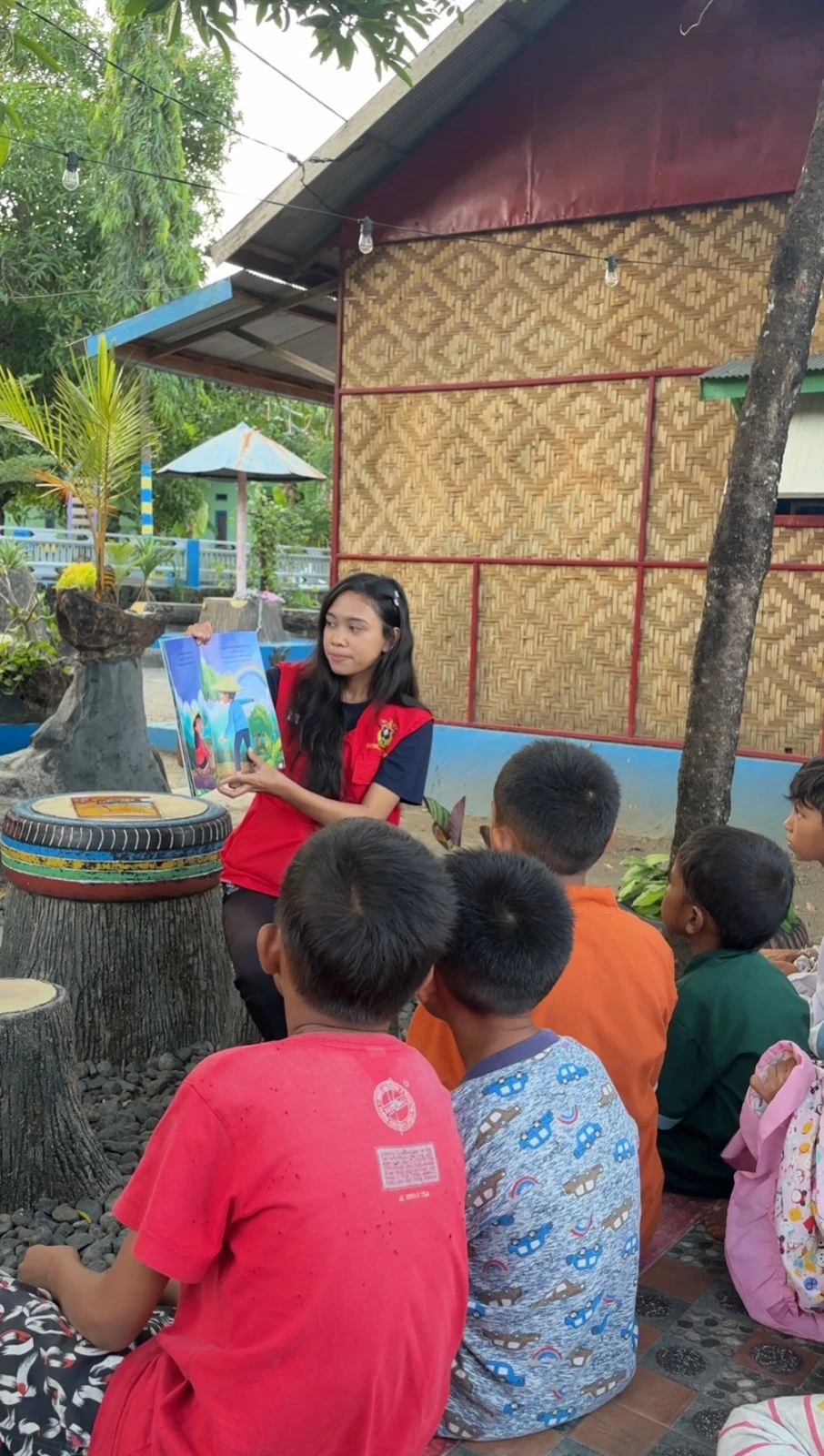 Seorang mahasiswa KKN Tematik Literasi Universitas Hasanuddin membacakan buku cerita bergambar secara nyaring kepada anak-anak Desa Gunung Silanu, Jeneponto, di Perpustakaan Al Fauzan (23/7). Kegiatan ini merupakan bagian dari kolaborasi Unhas dan Perpustakaan Nasional RI untuk menumbuhkan minat baca sejak dini melalui pendekatan interaktif dan penuh imajinasi, sekaligus memperingati Hari Anak Nasional 2024. Kredit: Mahasiswa KKN Gelombang 114.